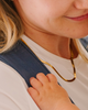 Mom wearing a gold necklace with her infant's hand on her chest