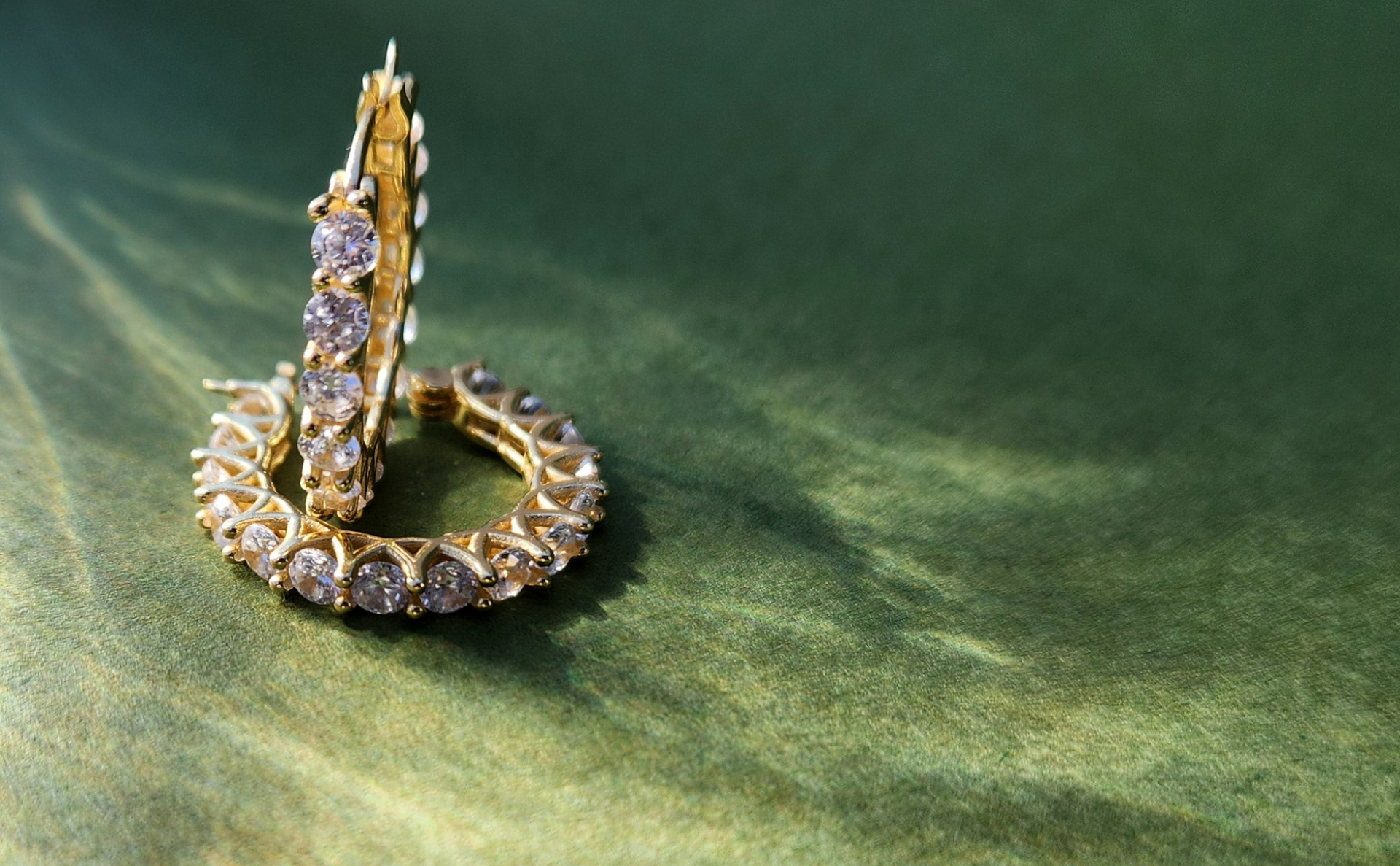 Gold hoop earrings with clear gemstones on a green background