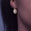 A close-up of a person's ear wearing a gold hoop earring adorned with small clear pavé stones.