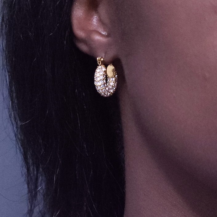 A close-up of a person's ear wearing a gold hoop earring adorned with small clear pavé stones.