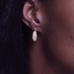 A close-up of a person's ear wearing a small gold hoop earring with a
 cluster of clear stones.