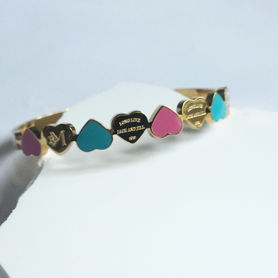 A gold-plated bangle bracelet with a series of colorful heart-shapes in pink and blue, displayed on a white surface.