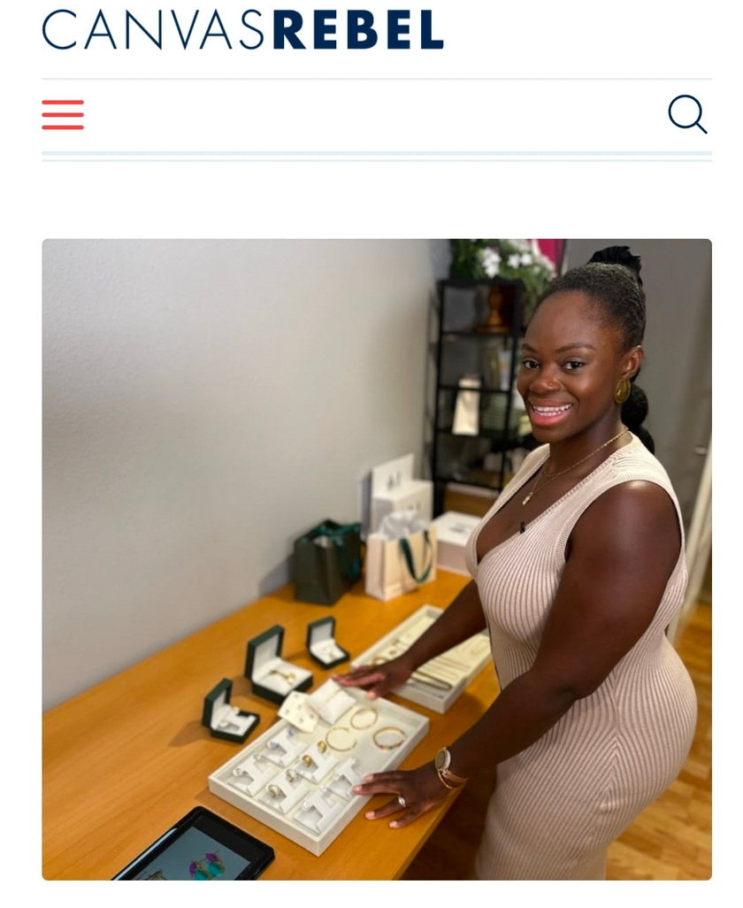 A woman in a beige ribbed dress stands behind a wooden display table filled with jewelry boxes and trays containing rings and bracelets, in an indoor retail or boutique setting. The Canvas Rebel logo appears at the top of the image.
