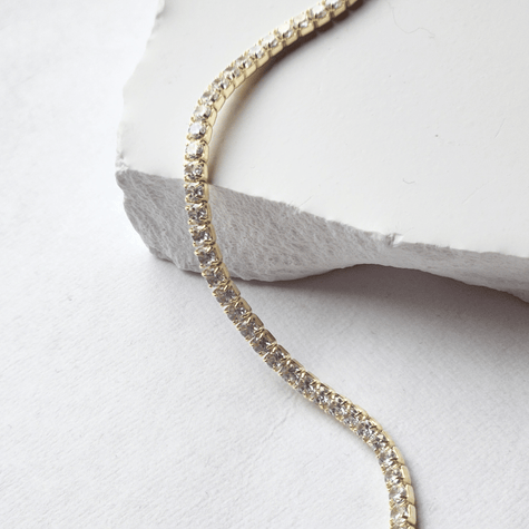Gold bracelet with clear stones on a white stone surface