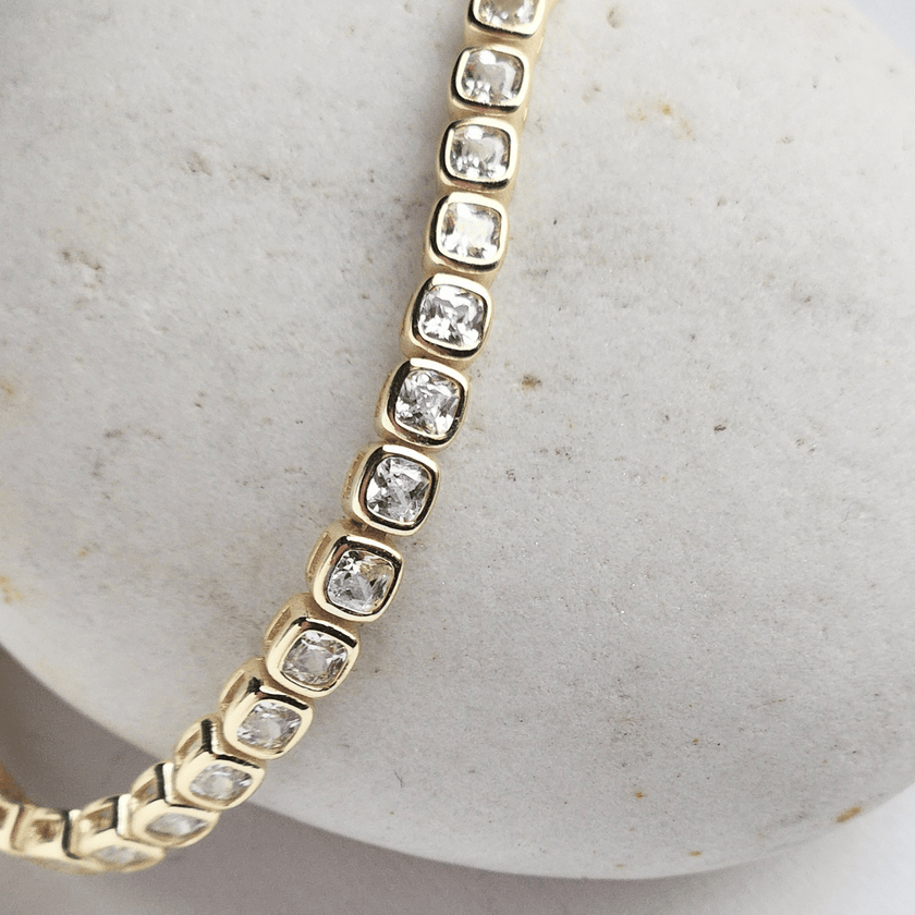 Gold bracelet with clear stones on a textured beige surface