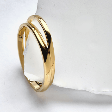 Two gold bracelets on a white stone surface
